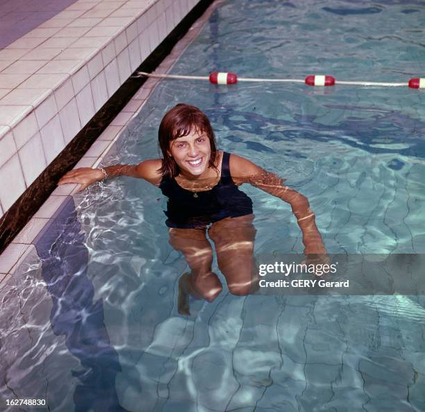 Kiki Caron. France- Années 65-66- Portrait de Christine CARON, dit Kiki CARON, nageuse française, souriante, dans l'eau, se tenant au rebord interne...
