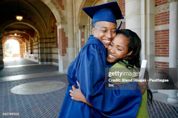 smiling black woman holding graduation diploma and hugging daughter - graduation stockfoto's en -beelden