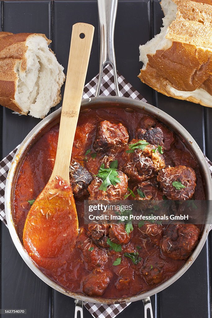 Pot of home made meatballs in sauce with parsley; wooden spoon; bread