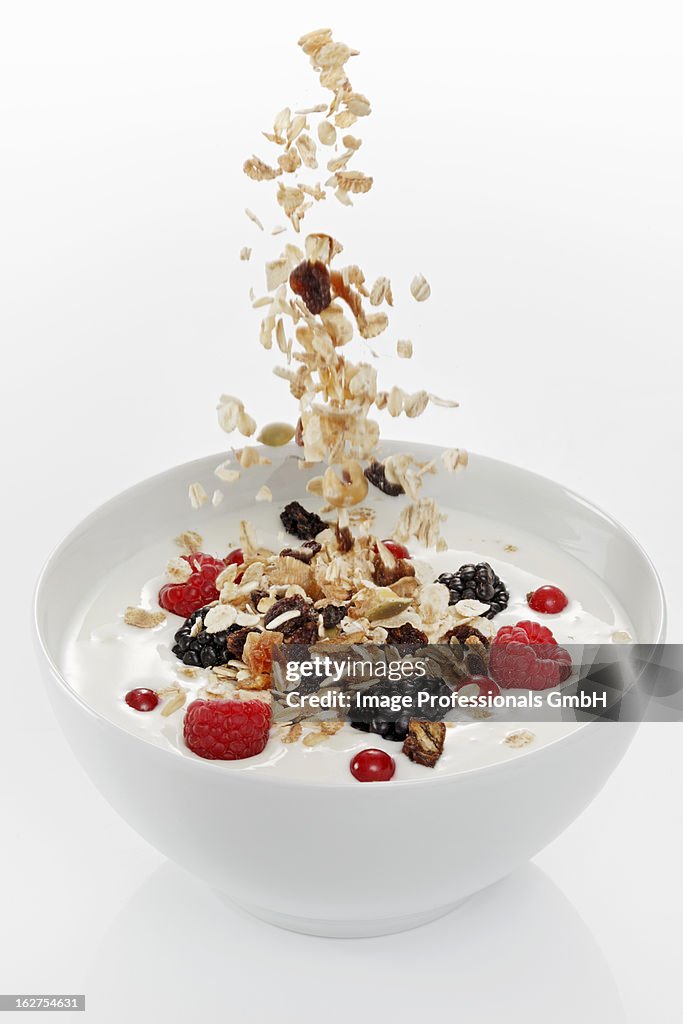 Cereals falling into yoghurt muesli with berries