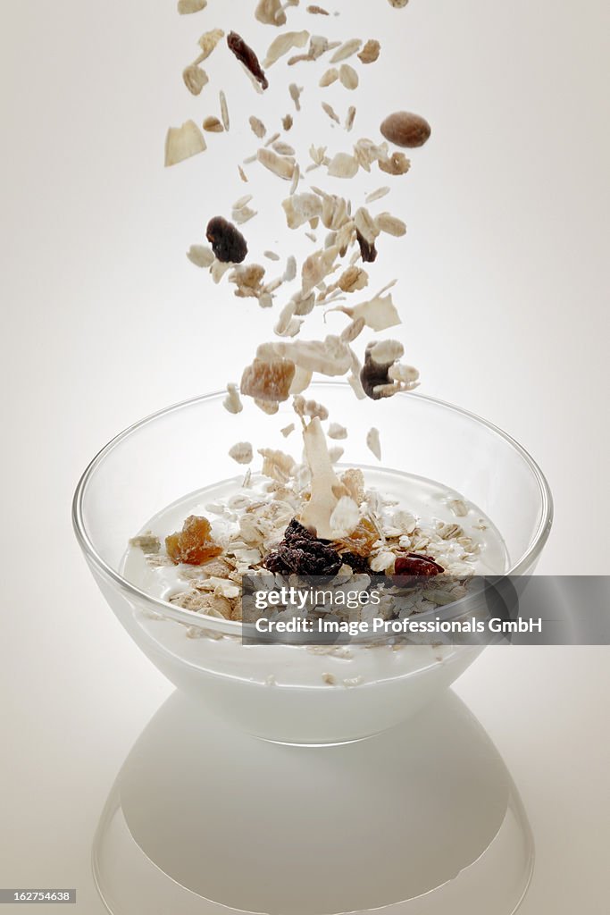 Muesli ingredients falling into bowl of yoghurt