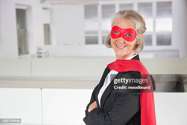 portrait of smiling senior businesswoman in superhero costume in office - roter anzug stock-fotos und bilder