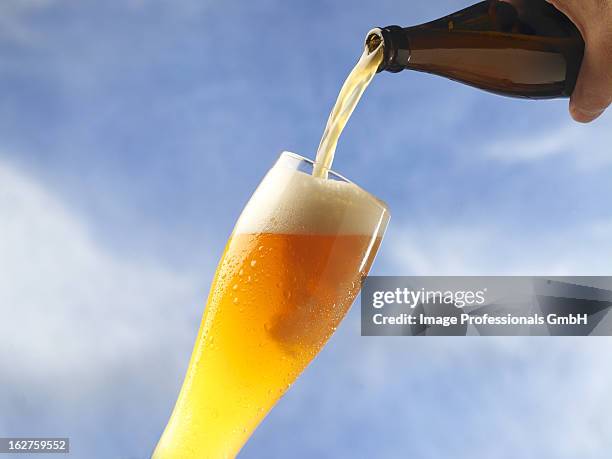 wheat beer being poured against sky - weizenbier stock-fotos und bilder