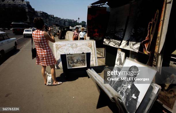 Tourism In Paris. A Paris en août 1971, une touriste de dos, photographiant deux enfants sur un quai de Seine, devant l'échoppe d'un bouquiniste,...