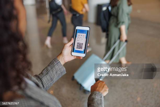 latin-american business woman looking at her digital boarding pass - phone screen at airport stockfoto's en -beelden