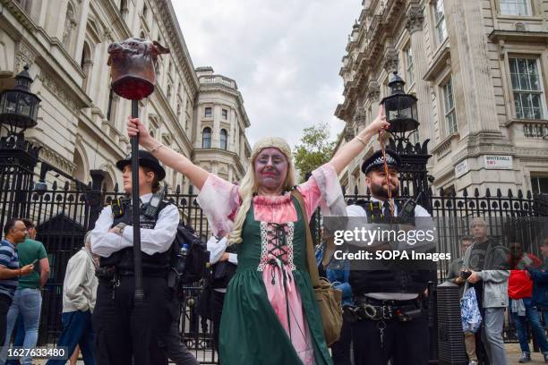 Protester wearing a costume and holding a fake pig's head stands next to police officers during the demonstration outside Downing Street. Crowds...