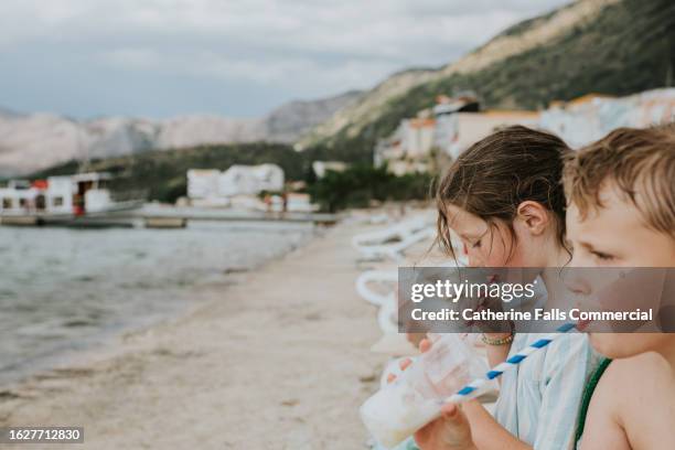 two children sit by the coast, drinking smoothies from takeaway plastic cups - balkans stock pictures, royalty-free photos & images