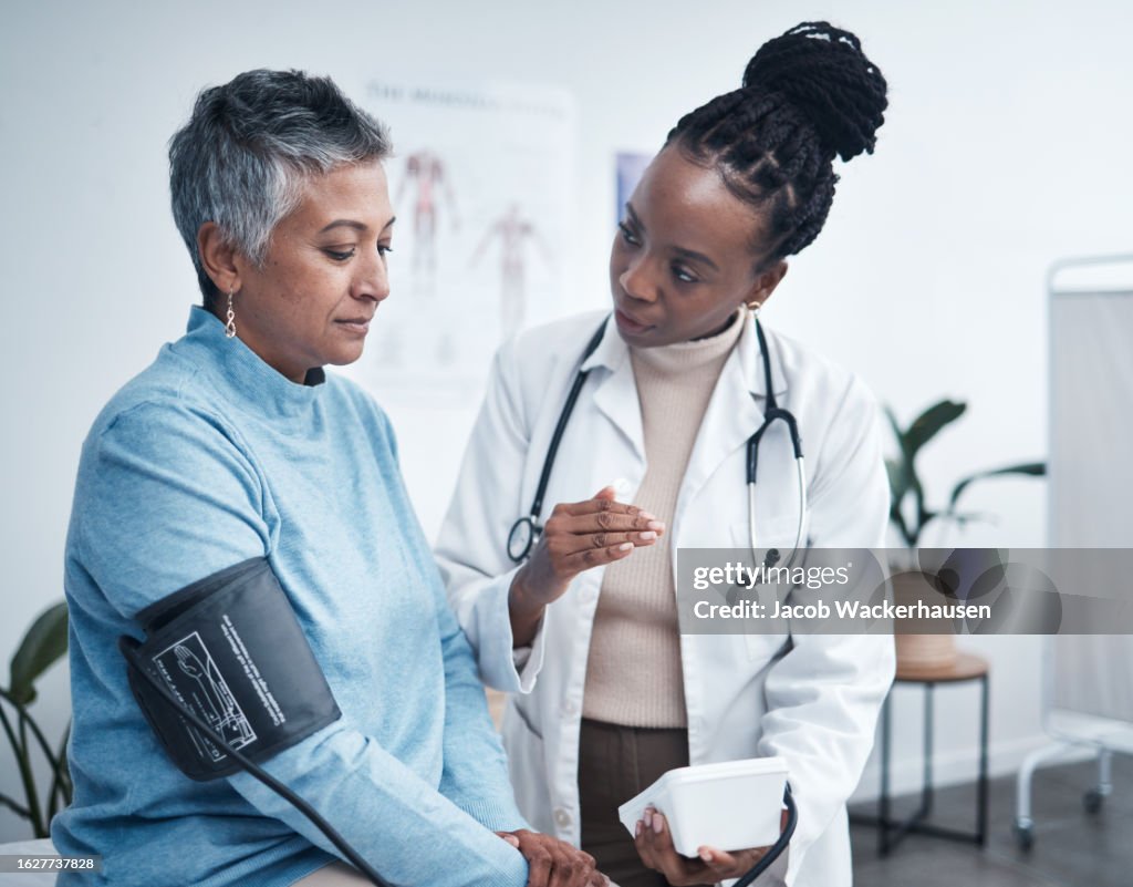 Black woman, doctor and senior patient with blood pressure reading for wellness, advice and conversation. Medic, elderly client and medical tools for health, cardiology and results in hospital office