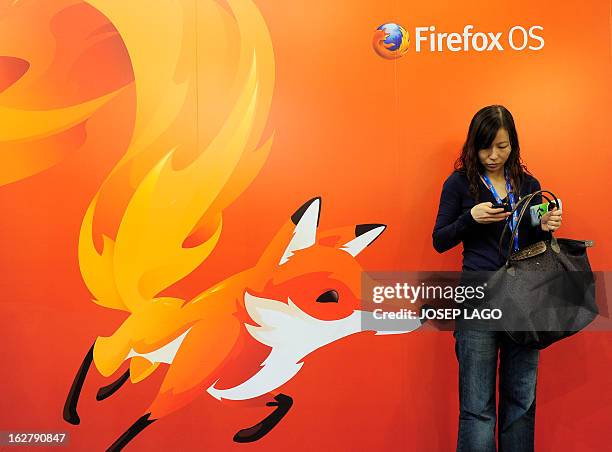 Woman looks at her mobile phone as she stands in front of a poster of Mozilla Firefox on February 27, 2013 at the Mobile World Congress, the world's...