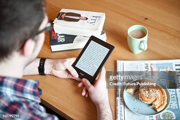 Close-up of a man using a Kindle Paperwhite e-reader whilst enjoying morning coffee, January 17, 2013.