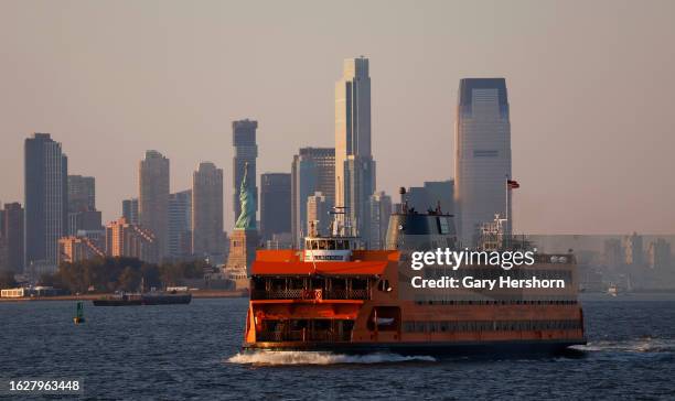 Staten Island Ferry sails past the skyline of Jersey City, New Jersey, and the Statue of Liberty as the sun sets on August 19 in New York City.