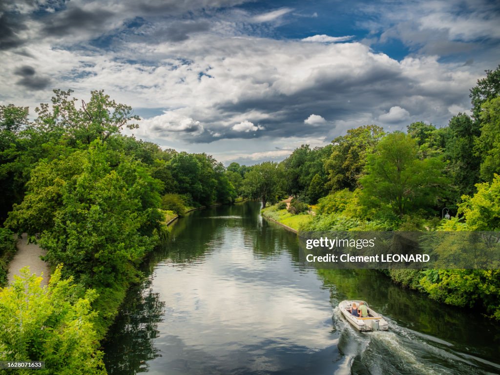 Small leisure boat in the Landwehr canal surrounded by trees and dense vegetation. Großer (Grosser) Tiergarten public park, Central Berlin, Germany.
