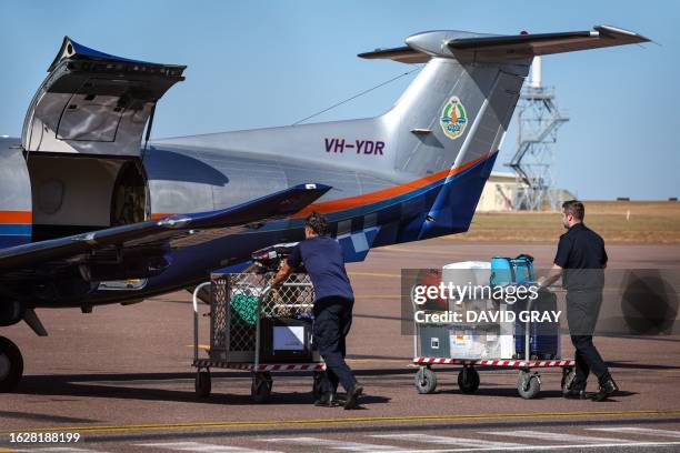 Police personnel push equipment on trolleys towards a Northern Territory Police on the tarmac of the Darwin International Airport in Darwin on August...