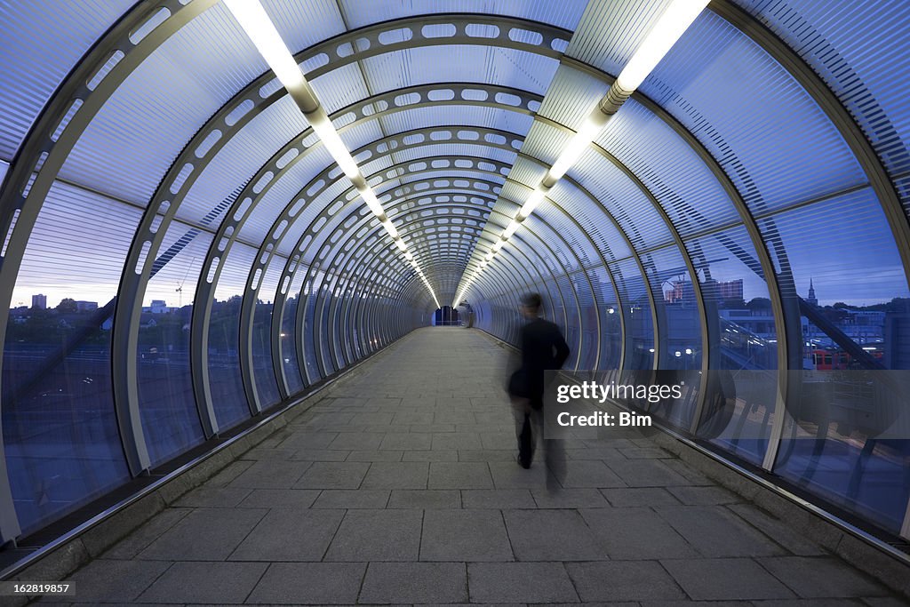 Geschäftsmann zu Fuß durch gläserne Fußgängerbrücke in der Dämmerung