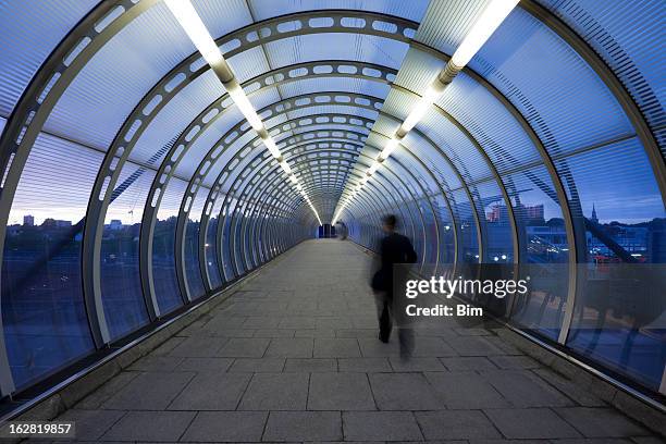 hombre de negocios caminando a través de un puente peatonal de cristal en crepúsculo - paso elevado fotografías e imágenes de stock