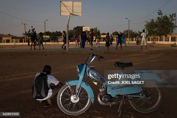 Boy sits next to a Motobecane motorcycle as he looks at young players of basketball at the former "Sharia Square" in central Gao on February 26,...