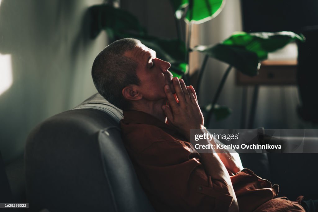 Unpleasant pain. Sad unhappy handsome man sitting on the sofa and holding his forehead while having headache