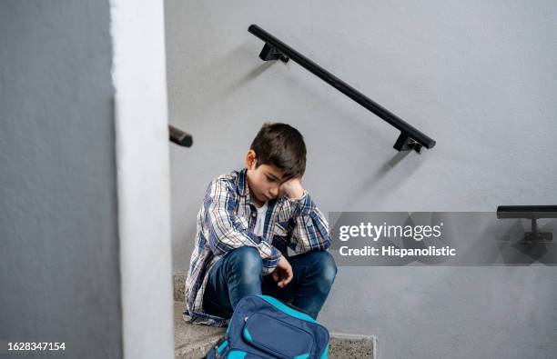 sad little boy sitting at the stairs of his school looking depressed and lonely - schoolboy stockfoto's en -beelden