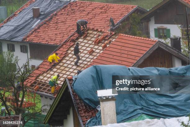 August 2023, Bavaria, Bad Bayersoien: People secure damaged roofs with tarpaulins and remove broken roof tiles. Thunderstorms caused havoc in...