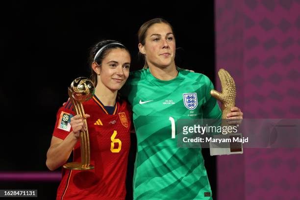 Spain's midfielder, Aitana Bonmati holding the trophy on the podium for the FIFA Golden Ball Award embraces England's goalkeeper Mary Earps holding...