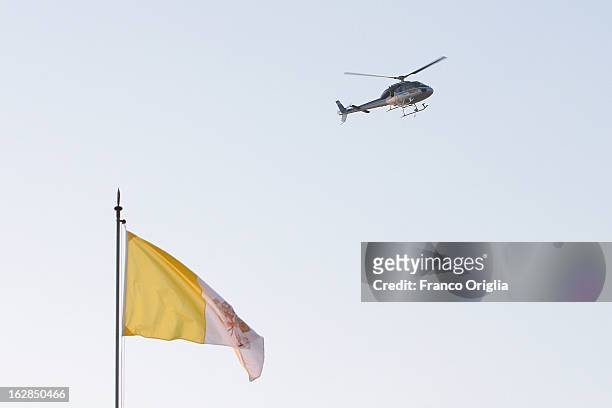 Surveillance helicopter flies over a Vatican flag in the main Square of Castel Gandolfo prior to Pope Benedict XVI last appearance at the Balcony of...