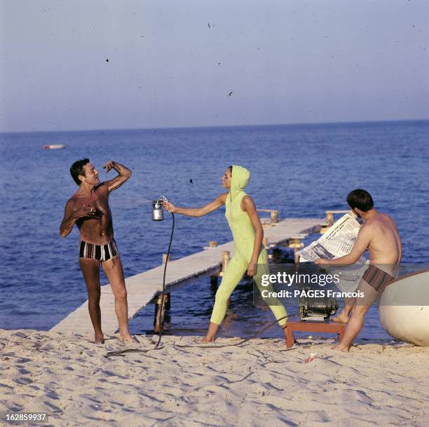 Nathalie Vadim. En France, sur une plage, Nathalie VADIM, en combinaison avec une capuche, aspergeant un homme en maillot de bain, avec un pistolet à...