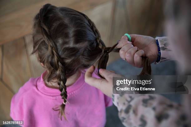 over the shoulder view of mother braiding a little girl's dark brown hair. - alpha female stock pictures, royalty-free photos & images