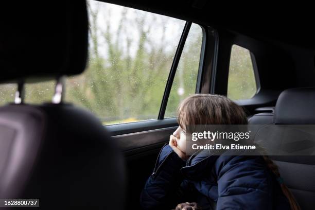 child sitting in the back of a parked car, leaning on elbow and looking out of the window with a bored expression. - alpha female stock pictures, royalty-free photos & images