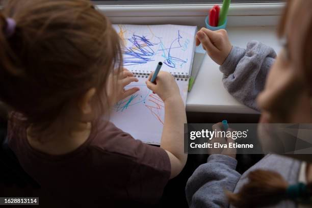 elevated view of two children using felt-tip pens to draw on a sketch pad on a window sill. - alpha female stock pictures, royalty-free photos & images