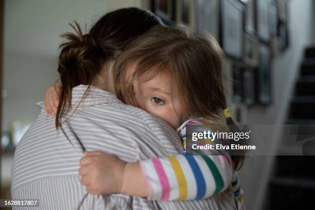 young girl gripping tightly to her mother in a reassuring embrace, with her arms wrapped around her mother's shoulders, in a domestic setting. - alpha female stock pictures, royalty-free photos & images