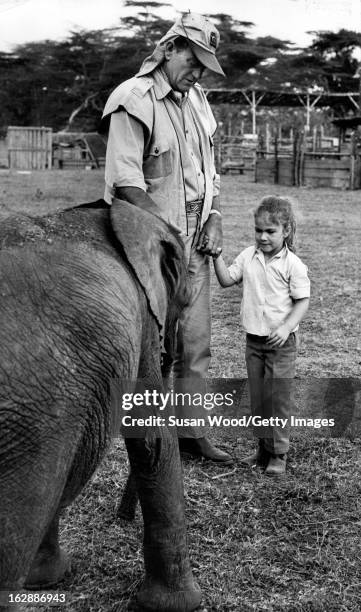 American actor John Wayne holds the hand on a young girl as he introduces her to a baby elephant during the filming of 'Hatari!' , Tanzania, 1962.