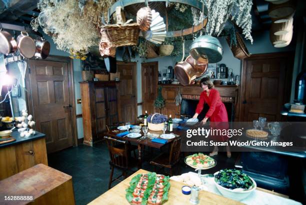 American media mogul and businesswoman Martha Stewart, in a red dress, sets the table in a kitchen, August 1976. On the table are plates, wine,...