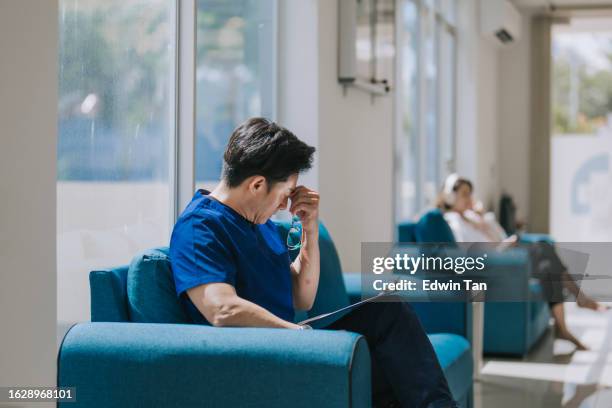 exhausted asian chinese male surgeon resting on sofa taking a break - stress test stockfoto's en -beelden