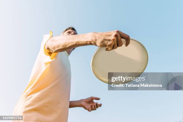 young man with flying disc frisbee in hands, bottom view, blue sky background. concept of sport in summer. - disc golf stock-fotos und bilder