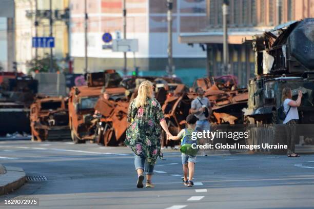 Woman and a child walk past destroyed Russian military equipment exhibited on Khreshchatyk Street in preparation for Independence Day on August 21,...