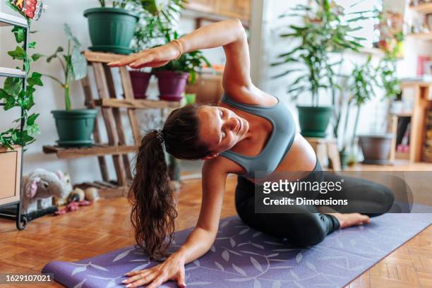 a pregnant woman doing a yoga pose at her apartment - prenatal yoga stock pictures, royalty-free photos & images