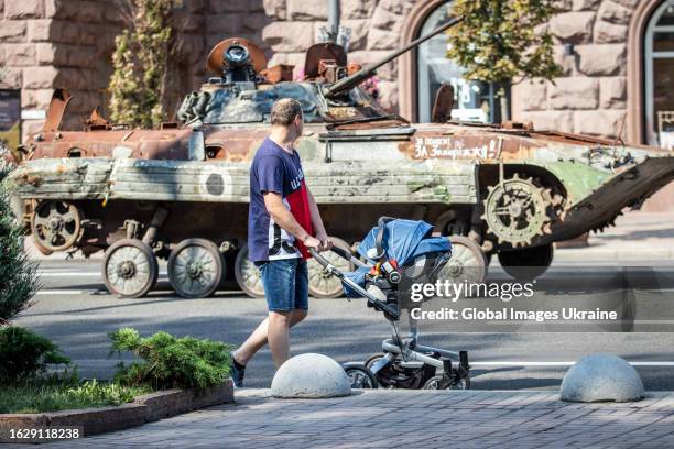 Man with a baby stroller walks past destroyed Russian military equipment exhibited on Khreshchatyk Street in preparation for Independence Day on...