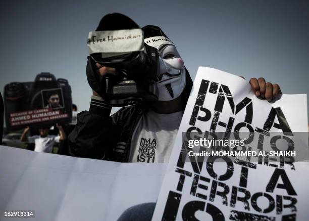 Bahraini protester wearing a Guy Fawkes mask used by the Anonymous movement holds a camera and a sign reading "I'm a photographer not a terrorist" to...