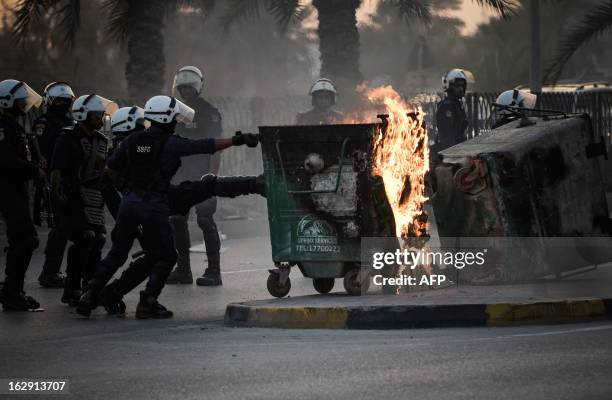 Bahraini riot policemen push burning trash containers that were set on fire by protesters to block a road during an anti-government demonstration in...