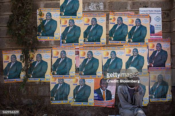 Worker wearing a safety helmet sits on a roadside in front of political election posters for Elias Otieno Okumu in Nairobi, Kenya, on Friday, March...