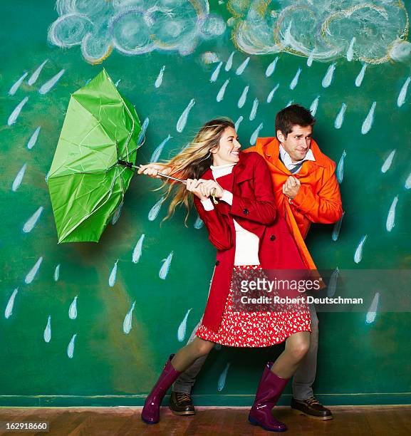 a young man and woman trudging through the rain. - sharing umbrella stock pictures, royalty-free photos & images