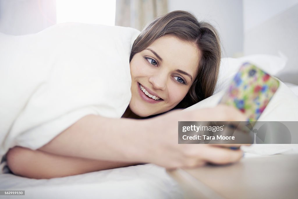 Woman smiling looking at mobile phone in bed