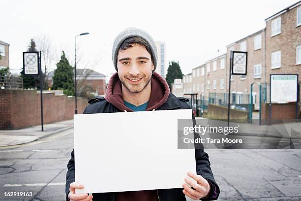 young man smiling to camera holding blank sign - schild halten stock-fotos und bilder