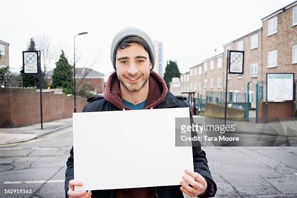 young man smiling to camera holding blank sign - person holding blank sign fotografías e imágenes de stock