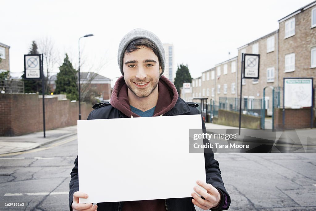 Young man smiling to camera holding blank sign