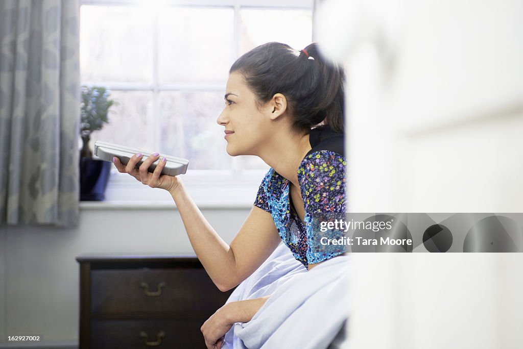 Woman lying on bed using tv remote control