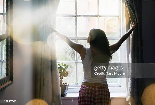 woman opening curtains in the morning - tagesablauf stock-fotos und bilder