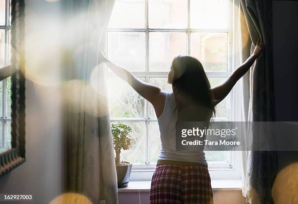 woman opening curtains in the morning - awake day stockfoto's en -beelden