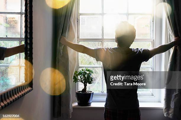 man opening curtains in the morning - in den zwanzigern stock-fotos und bilder