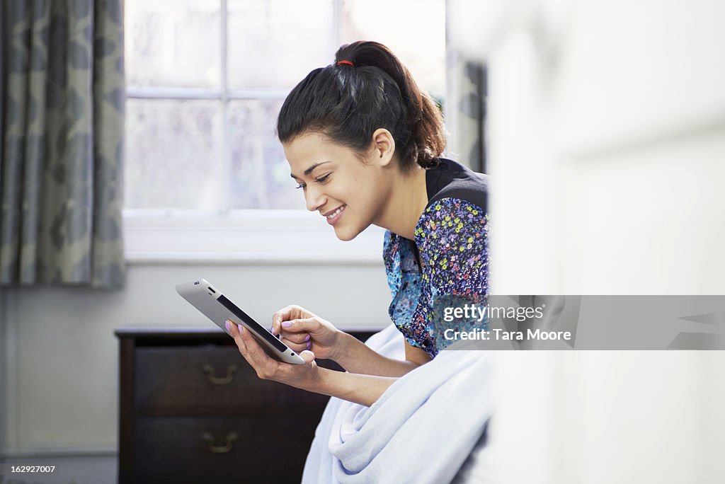 Woman lying on bed looking at digital tablet